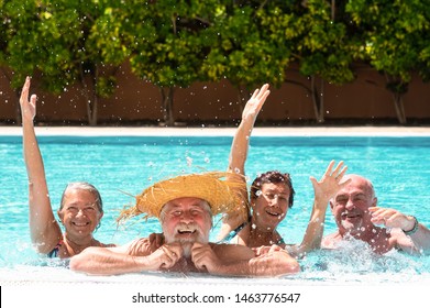 Four Senior People Friends Laughing Enjoying The Swimming Pool Together. Bright Sunlight And Transparent Water. Large Smiles And Happiness. Floating In The Water