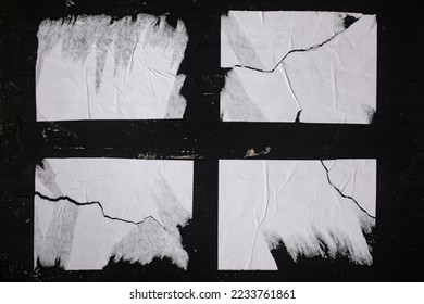 Four sheets of white torn paper on a black wall.