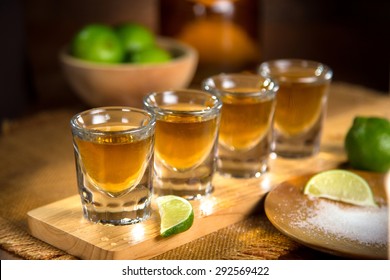 Four shot glasses with tequila bottle and bowl of limes with salt at a bar
