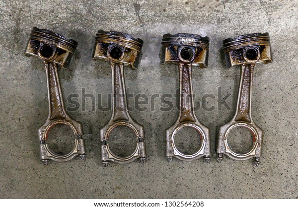 Four silvery metal car\
pistons in poor condition removed from the used engine in a deposit\
of oil lying on concrete in a vehicle repair shop for washing and\
restoration
