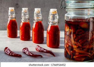 Four Small Bottles Of Chili Hot Sauce Made From Fermented Dry De Cayenne Chilies. Jar With Fermentation Process And Dry Chilies In Front.