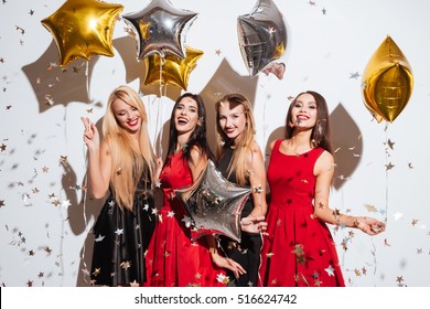 Four smiling attractive young women with star shaped balloons and confetti dancing and having party over white background