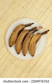 Four Steamed Saba Bananas Served On White Plate With Rattan Mat Background. 