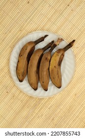 Four Steamed Saba Bananas Served On White Plate With Rattan Mat Background.