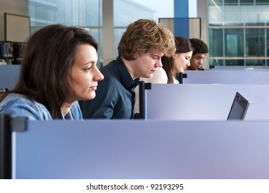 Four Students In A Row, Separated By Desk Dividers, Studying In A Library, With Focus On The Second Man