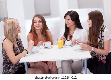Four stylish attractive young female friends seated at a table chatting over coffee