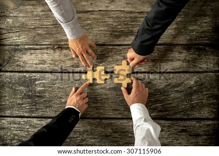 Four successful business men joining two puzzle pieces each being held by two partners, rustic wooden background. Conceptual of merger or creative cooperation of two business companies.
