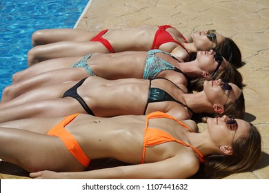 Four sunbathing women in sexy bikinis lying close together on the tile by the swimming pool