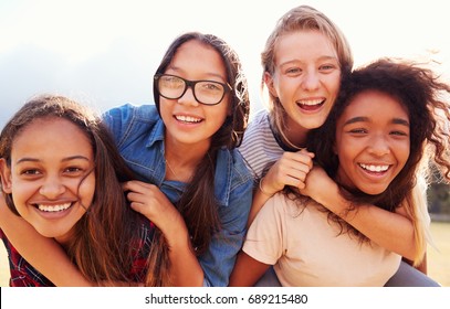 Four teenage girls having fun piggybacking outdoors
