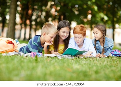 Four Teenage School Friends Reading Together Story For Literature Class In Park Lying On Grass After Classes At School