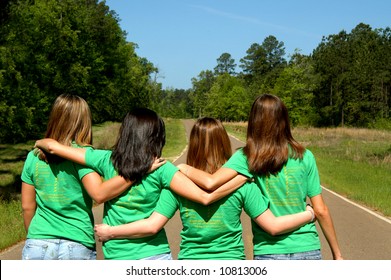 Four Teens Dressed In Matching Green Tee Shirts Walk Down A Highway Together Arms Locked.