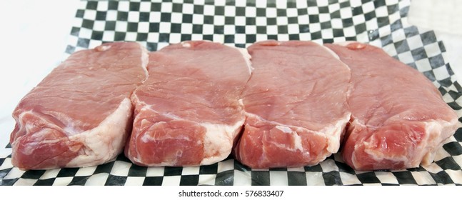 Four Thick Center Cut Pork Chops On Black And White Checkered Butcher Paper. Isolated.