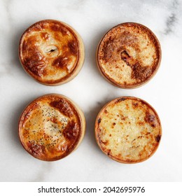 Four Traditional Hot Baked Meat Pies With Golden Pastry Crusts On White Marble Kitchen Counter  Background From Overhead Flat Lay View 