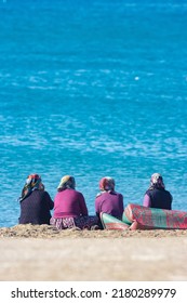 Four turkish vilage women in national authentic costume and headscarf sits on the carpet at the coast of sea beach