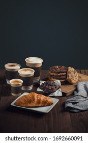 four types of coffee, espresso, cappuccino, latte and mokiyato in disposable take-away cups with pastries on one table, croissant and chocolate shortbread cookies