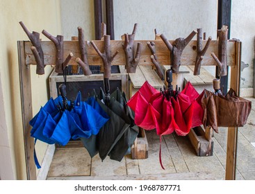 Four Umbrellas Of Different Colors Hang On A Coat Rack Made From Recycled Wood.