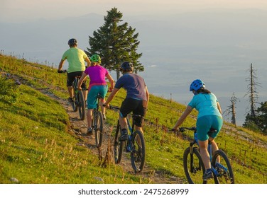 Four unrecognizable friends riding their mountain bikes uphill on a sunny summer morning. Active tourists pedalling electric mountain bicycles up a narrow dirt track in the beautiful green mountains. - Powered by Shutterstock