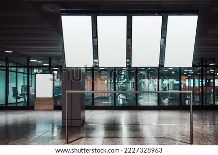 Four vertically oriented blank mock-ups of tv screens of a departure and arrivial board, and a template of an indoor ad billboard aloof near a glass wall of an airport or a train station waiting hall