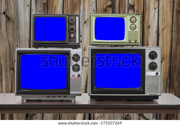 Four vintage televisions with old wood wall and\
chroma key blue screens.
