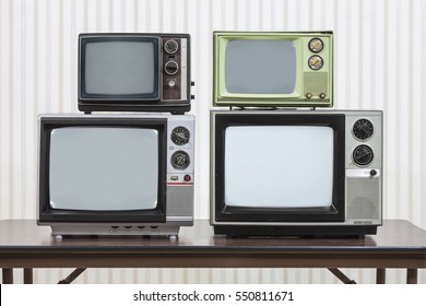 Four vintage televisions stacked on table.