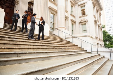 Four well dressed professionals in discussion on the exterior steps of a building. Could be lawyers, government workers, business people etc.
