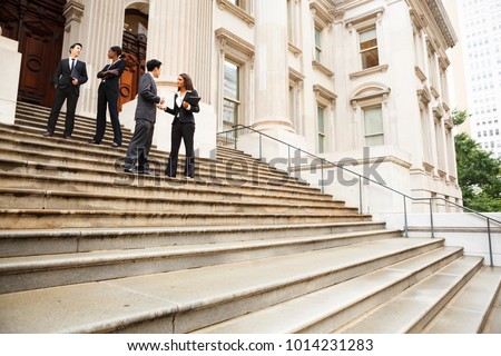 Four well dressed professionals in discussion on the exterior steps of a building. Could be lawyers, government workers, business people etc.
