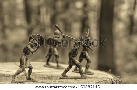 Four well-armed attacking Vikings (plastic toy soldiers), wooden surface,  Old Norse, Odin and Valhalla myths, monochrome image in sepia style, selective focus, blurred forest background
