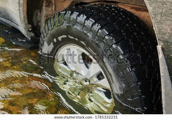 Four wheel drive agricultural\
vehicle crosses a flooded forded stream in nation park s\
forest.