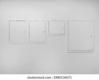 Four white electric meter boxes of different sizes on a white wall.	