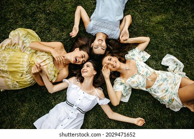 Four women best friends lying on grass, having good time, laughing.