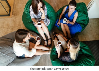 Four Women On A Break Drinking Coffee Sitting On A Bean Bag In The Office