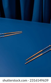 Four wooden chopsticks artfully arranged against a deep blue background with a blue curtain. Ideal for an Asian restaurant menu or a modern still life setting.