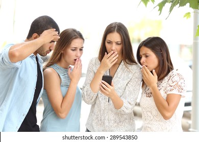 Four Worried Multi Ethnic Friends Watching A Smart Phone In The Street