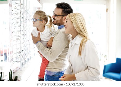 Four year little girl in optics store choosing glasses with her father. Ophtamologist helping. 