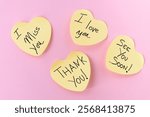 Four yellow, heart-shaped Post-It notes with handwritten messages: "I love you," "I miss you," "Thank you," and "See you soon," arranged on a pastel pink background.