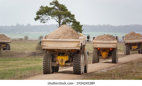 Four Yellow Volvo A40E And A40F Articulated Dump Truck Earth Movers Each Fully Laden With 25 Tonne Payload Kick Up Clouds Of Dust As They Convoy Across Salisbury Plain, Wiltshire UK