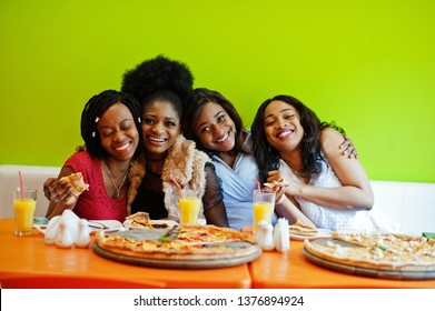 Four young african girls in bright colored restaurant eating pizza and having fun together.