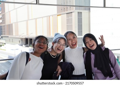 Four young attractive Asian group woman friends colleagues students talk walk discuss mingle outdoors backpack handphone outdoor notebook urban building cityscape look happy