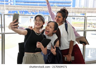 Four young attractive Asian group woman friends colleagues students talk walk discuss mingle outdoors backpack handphone outdoor notebook urban building cityscape taking selfie happy fun