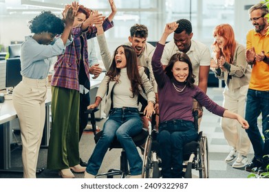 Four young diverse cheerful coworkers enjoying office chair race at workspace and having fun.Multiracial employees laughing and enjoying funny activity at work. Other colleagues cheering for them. - Powered by Shutterstock