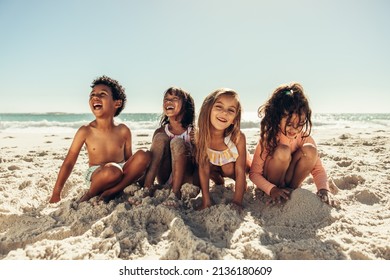 Four young friends laughing cheerfully while playing with sea sand at the beach. Group of adorable little kids having a good time together during summer vacation.