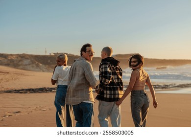 Four young friends walking along a sandy beach at sunset, enjoying the carefree vibes of summer - Powered by Shutterstock