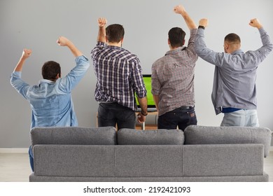 Four young men supporting their favourite team while watching live football game on television at home, back, rear view. Group of 4 fans stand up from couch while watching exciting soccer - Powered by Shutterstock