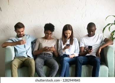 Four young people attractive girls guys sitting together on couch ignoring each other holding gadgets absorbed by smartphones. Bad habit, mobile phone overuse modern technologies dependency concept