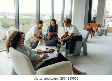 Four young professionals engage in a collaborative meeting in a contemporary office, with one woman focused on her laptop while others share ideas