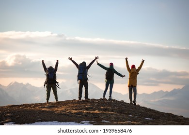 Four young tourists with backpacks in winner poses at mountain top