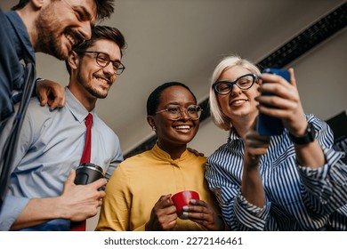 Four young women and men use a mobile cell while having fun in the office. Connecting with millennial people through online platforms. Social media - Powered by Shutterstock