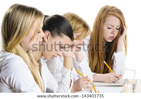 Four young women sitting at a table and write a focused examination, isolated against white background.