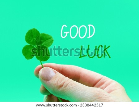 Four-leaf clover in a hand, isolated on a green background. 'Good luck' card. Concept St. patricks day, success,...