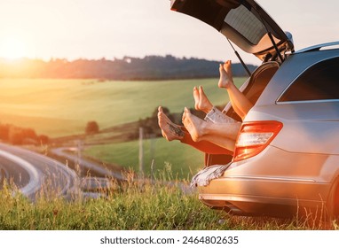 Four-person family lying in the car trunk and fooling around raising feet up. The young caucasian couple has an auto trip break. Family values, traveling, and friendship concept. - Powered by Shutterstock